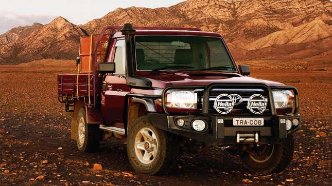 A photo of a red Toyota Land Cruiser pickup truck in the mountains. 