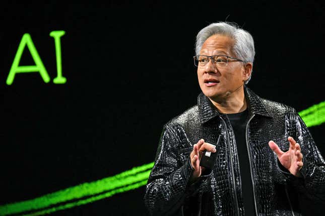 Jensen Huang speaking with his hands up wearing a black t shirt and shiny black crocodile leather jacket in front of a black backdrop with the letters AI in neon green