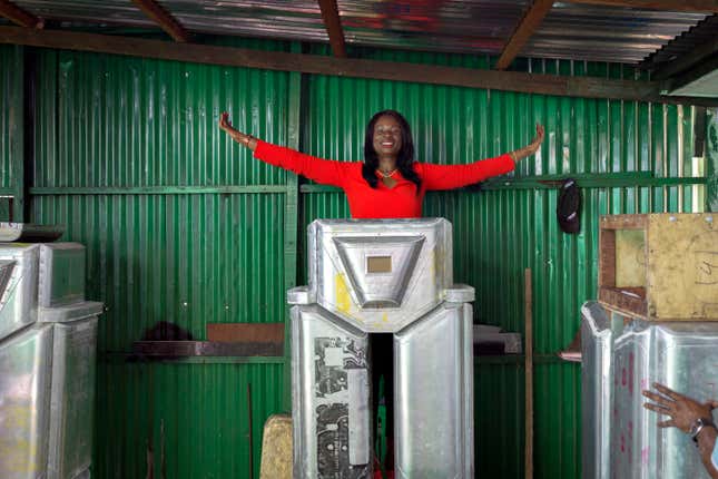 Therese Kirongozi, the president of Women’s Tech, poses above a half-completed humanoid robocop in her workshop.