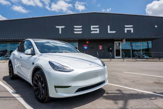 a white Tesla sits in an empty parking lot in front of a Tesla sign