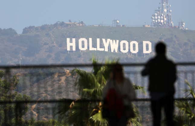 Two people silhouetted in the foreground look out at the iconic Hollywood sign. 