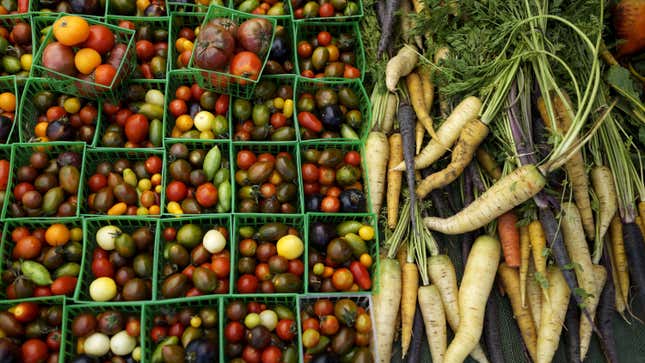 Contenedores de tomates y montones de zanahorias sueltas en un mercado de agricultores