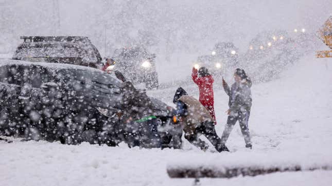 People push and photograph their car stuck in the snow along Sierra Highway on February 25, 2023 near Acton, California.