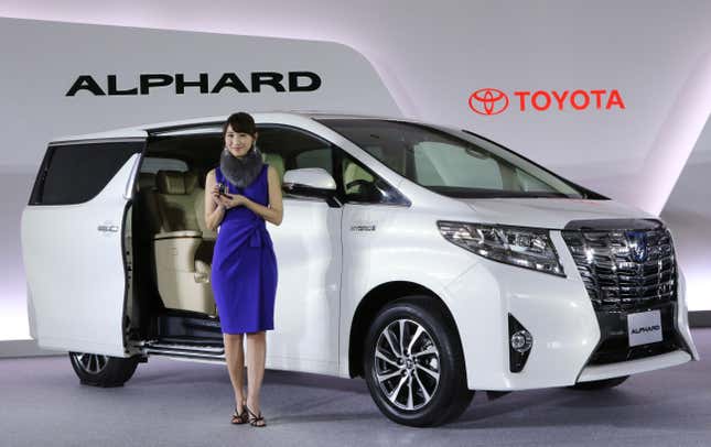 Un Toyota Alphard blanco en una exhibición del automóvil con un modelo parado frente a él 