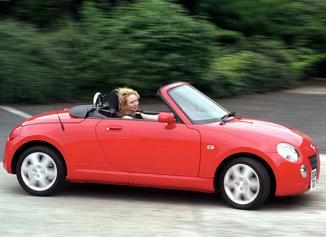 An adorable red Daihatsu Copen being driven by a blonde woman with the top down and her hair blowing