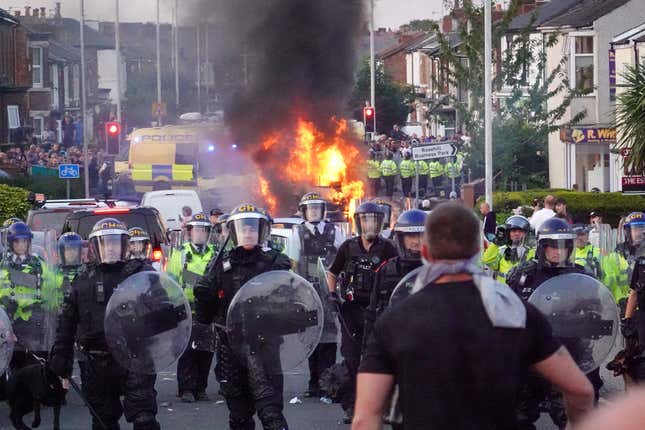 Riot police hold back protesters near a burning police vehicle after disorder broke out on July 30, 2024 in Southport, England