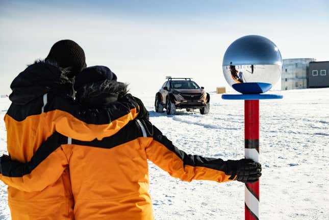 The couple touching the South Pole and looking back at their Ariya.