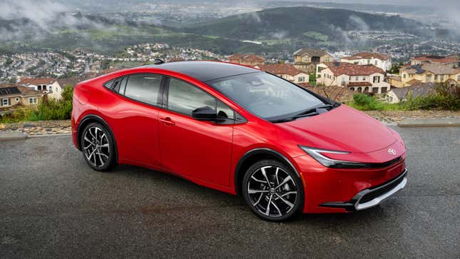 A red Toyota Prius on a road overlooking a residential area.