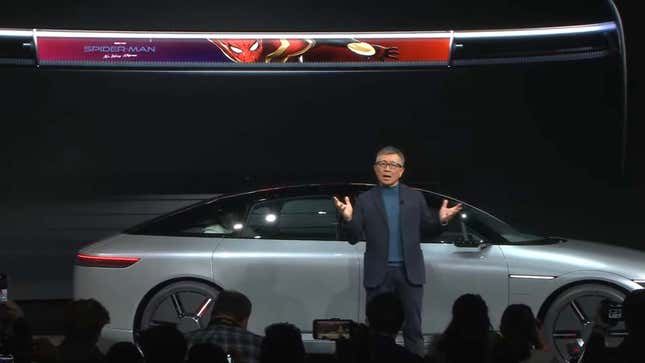 A man stands on stage and shows off the new Sony smart car and its media bar. 