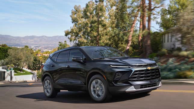 a black chevy blazer driving up a hill with trees and mountains in the background