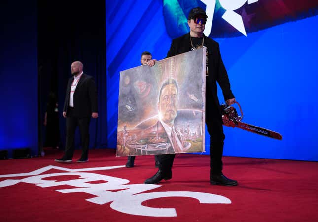 Elon Musk holds a chainsaw and a painting of himself as he leaves the stage after speaking at the Conservative Political Action Conference on February 20, 2025. 