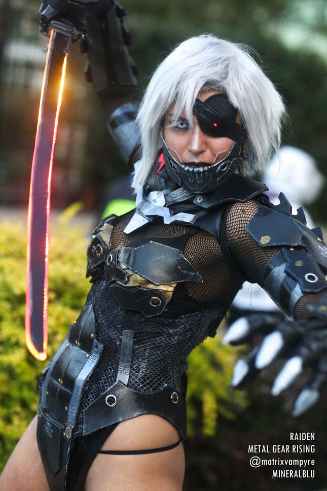 A cosplayer dressed as Raiden from Metal Gear Rising wields a glowing red sword.