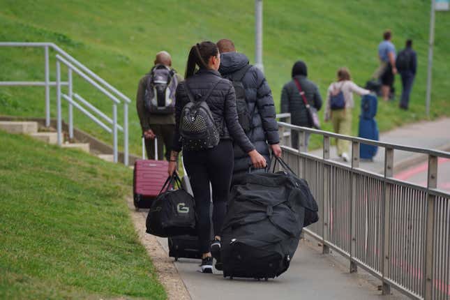 Passengers carry their luggage along a pathway at Luton Airport, England, Wednesday, Oct. 11, 2023. Thousands of travelers faced disruption as all flights were suspended on Wednesday at London&#39;s Luton airport after a fire tore through a newly built parking garage, destroying vehicles and partially collapsing the structure. (Lucy North/PA via AP)