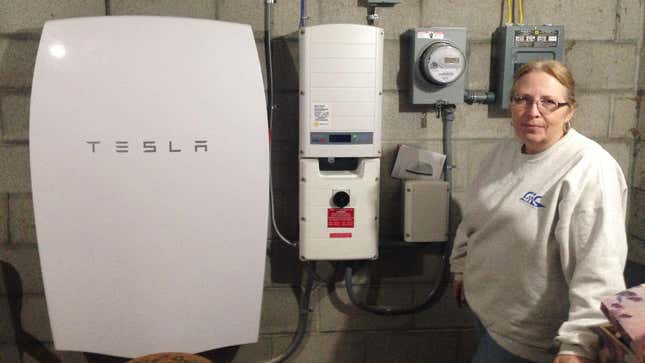 Rhonda "Honey" Phillips poses next to a Tesla Powerwall battery and inverter connected to a solar panel array in her yard in Middletown Springs