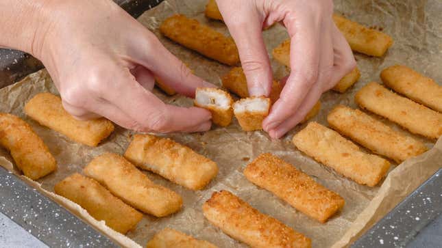 A pair of hands holding a broken open fish stick within a baking span full of cooked fish sticks.