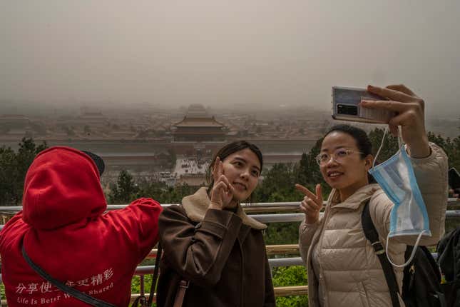 Chinese tourists take their photo with the Forbidden City in the background from Jingshan Park during a sandstorm on March 28, 2021 in Beijing, China. China's capital and the northern part of the country was hit with a sandstorm Sunday, sending air quality indexes of PM 2.5 and PM 10 ratings into the thousands for the second time in as many weeks.