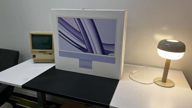 The box for a purple Apple iMac on top of a desk. 