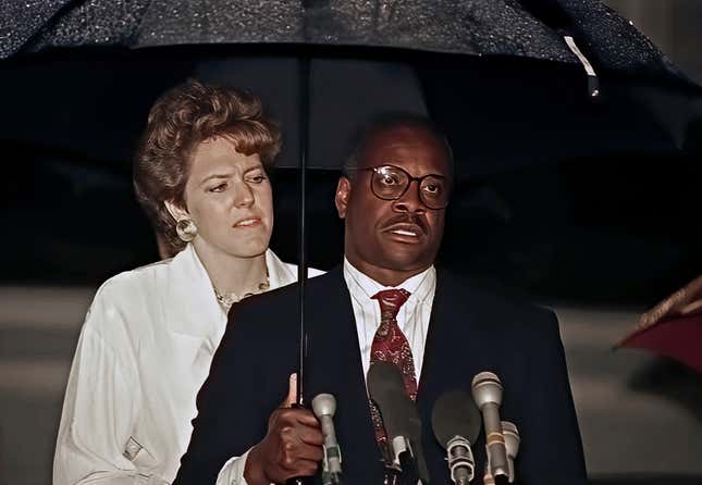 Under an umbrella, American attorney &amp; US Chamber of Commerce consultant Virginia Thomas stands behind her husband, Associate Justice of the United States Supreme Court Clarence Thomas, as the latter confirms his nomination (by the Senate Judiciary Committee) during a press conference outside their home, Alexandria, Virginia, October 15, 1991