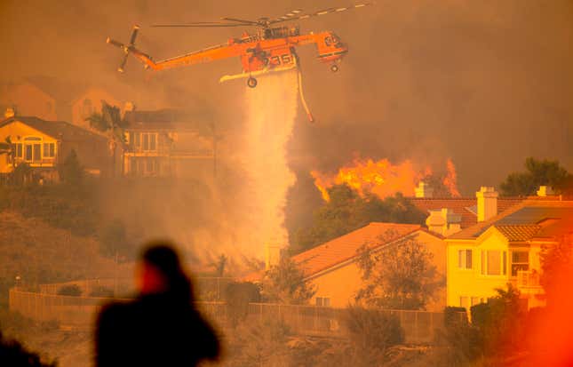 A helicopter drops water to help fight flames as the Saddleridge Fire in the Porter Ranch section of Los Angeles, California on October 11, 2019. 