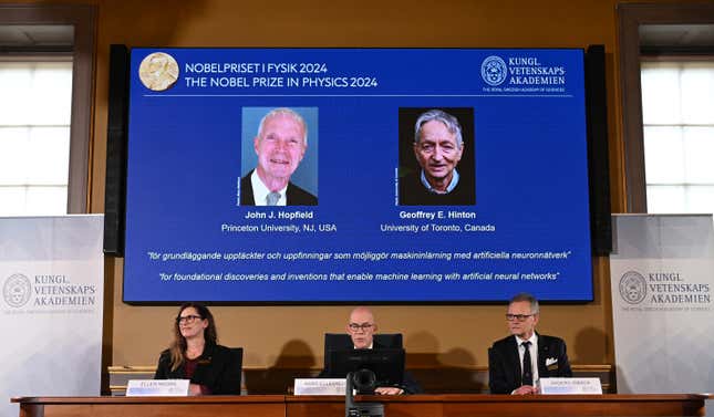 A screen shows the laureates of the 2024 Nobel Prize in Physics above a panel of three people