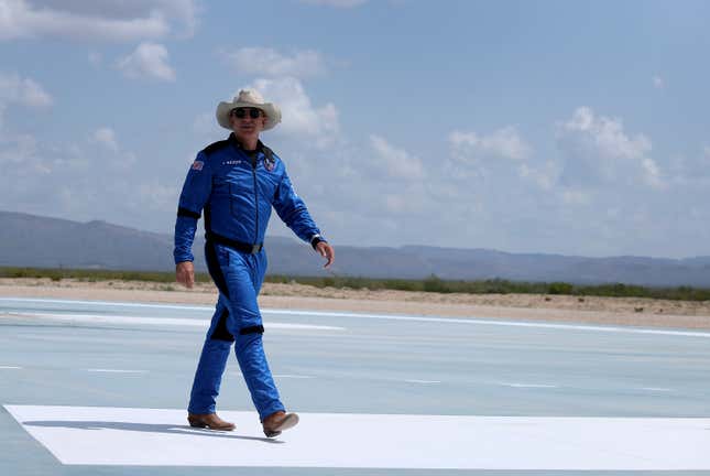 Jeff Bezos is wearing space gear and a cowboy hat and is walking on a tarmac. 
