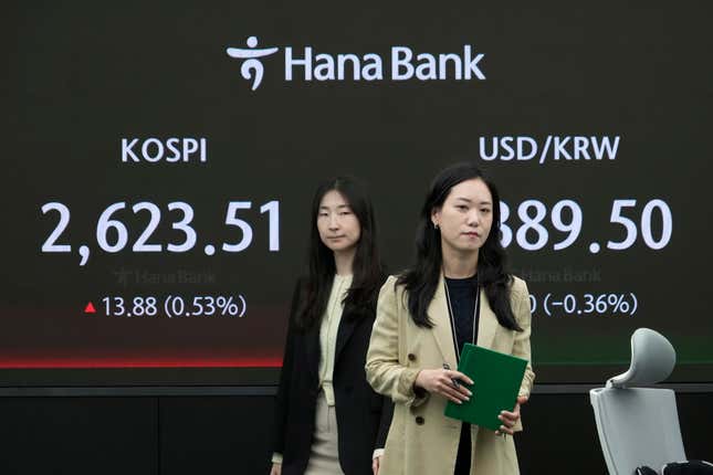 Currency traders pass by the screen showing the Korea Composite Stock Price Index (KOSPI), left, and the foreign exchange rate between U.S. dollar and South Korean won at the foreign exchange dealing room of the KEB Hana Bank headquarters in Seoul, South Korea, Wednesday, April 17, 2024. (AP Photo/Ahn Young-joon)