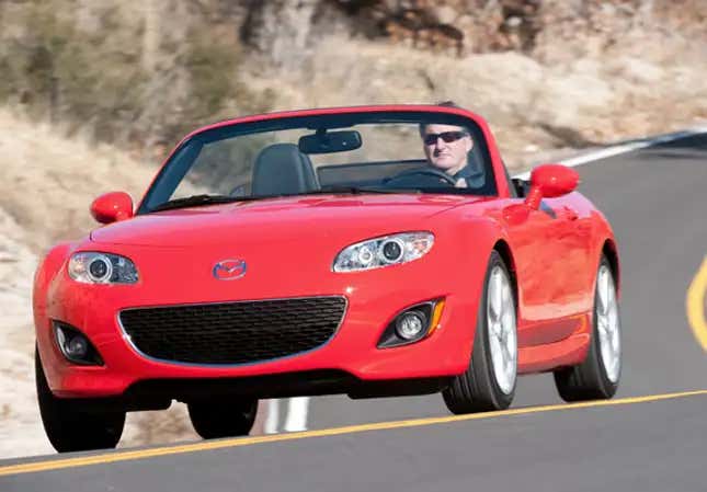 A red NC generation Mazda Miata drives on a canyon road.