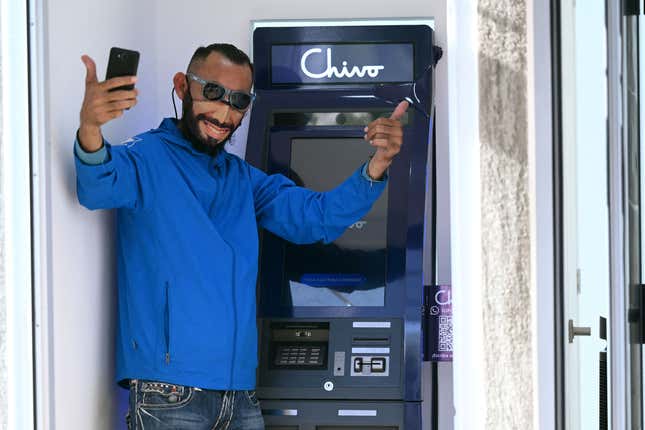 A man wearing a protective face mask with the image of Salvadoran  President Nayib Bukele pose for a picture at a bitcoin ATM in San  Salvador, on September 7, 2021.