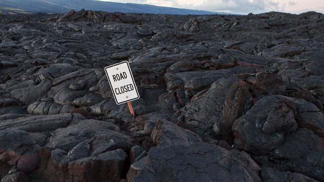 A photo of a Road Closed sign surrounded by lava. 