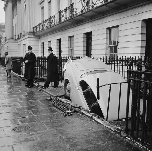 Two police officers inspect a Jaguar car which crashed into the a basement of a property on the Outer Circle of Regent's Park in London, England, 12th December 1961.