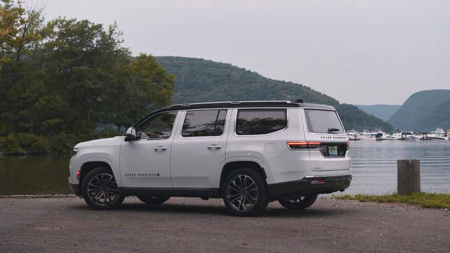 A photo of a white Grand Wagoneer SUV by a lake. 