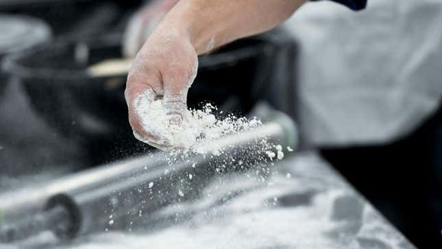 Person sprinkling flour across working surface