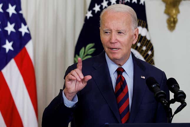 Biden delivers a speech at a podium in the White House. One hand is lifted with one finger pointed as he speaks.