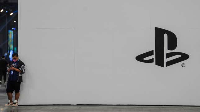 A man looks down at his phone standing alongside a large white wall sporting the Playstation logo.