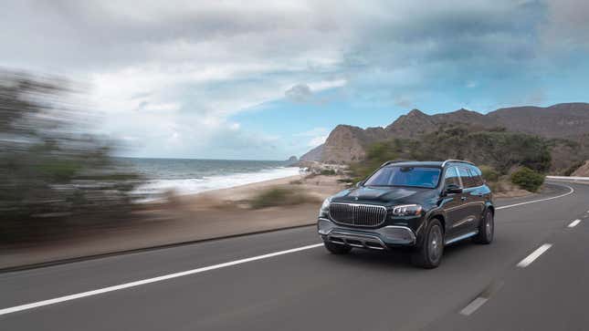 A photo of a dark green Mercedes SUV driving on a coastal road. 