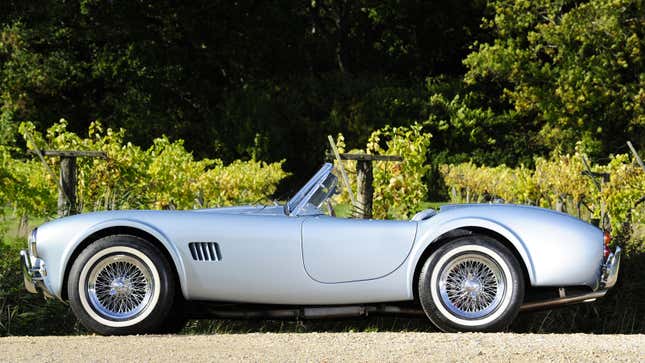 A side profile photo of a silver AC Cobra sports car. 