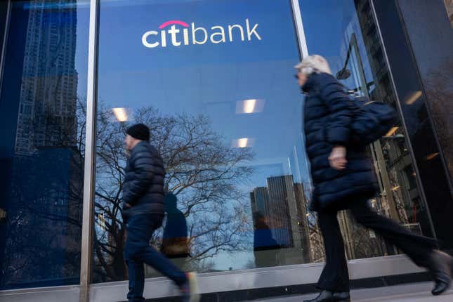 Two people walk past a Citibank logo on a building window