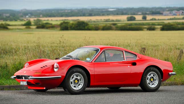 A photo of a red Ferrari 246 parked near a field. 