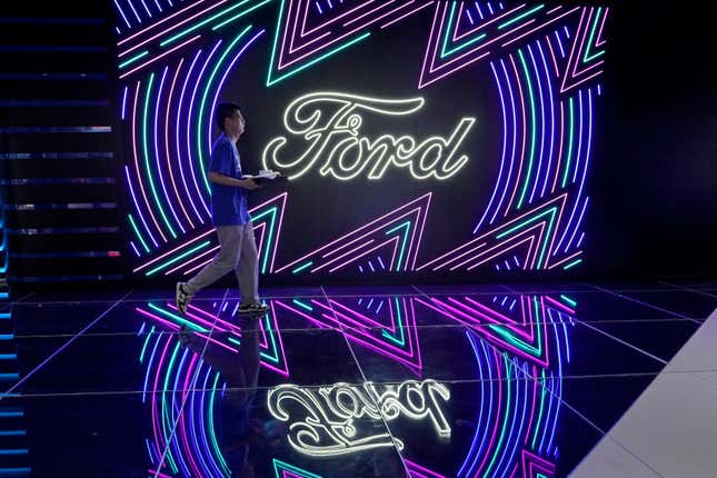 FILE - A worker walks past neon signs for Ford at the Auto Shanghai 2023 show in Shanghai, Tuesday, April 18, 2023. Ford reports their earnings on Wednesday, April 24, 2024. (AP Photo/Ng Han Guan, File)