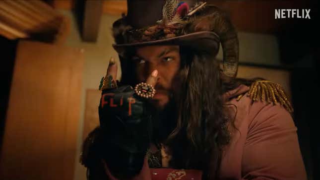 Jason Momoa, in a purple top hat, suit, and satyr horns, flips the "metal" sign.