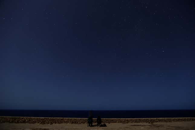 A meteor streaks past stars as people face the sea hoping to catch a glimpse of shooting stars during the Perseid meteor shower at Migra l-Ferha, outside the town of Rabat.
