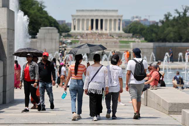 Visitors and tourists to the World War II Memorial shade themselves under umbrellas as temperatures reach into the 90's on July 03, 2023 in Washington, DC. Due to extreme temperatures and high humidity Washington, DC has declared a heat emergency urging residents to take precautions outside and to stay hydrated.