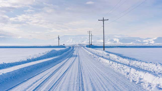 Carretera cubierta de nieve a través de praderas de invierno con montañas en la distancia y líneas eléctricas a lo largo de la carretera