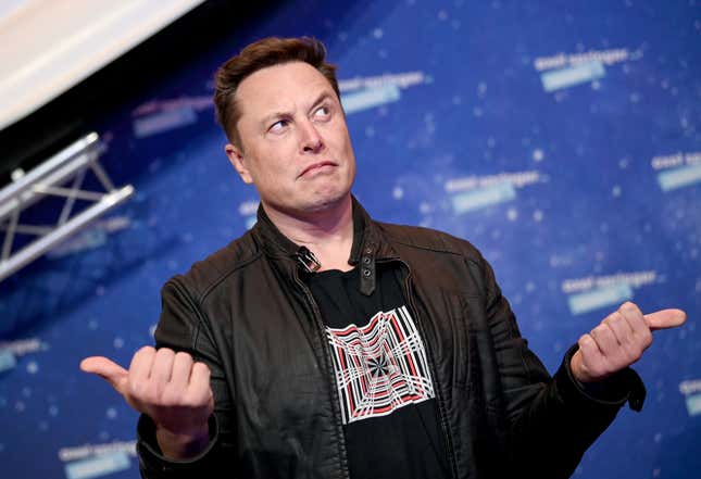 Elon Musk with an ironic look on his face pointing both thumbs to either side.