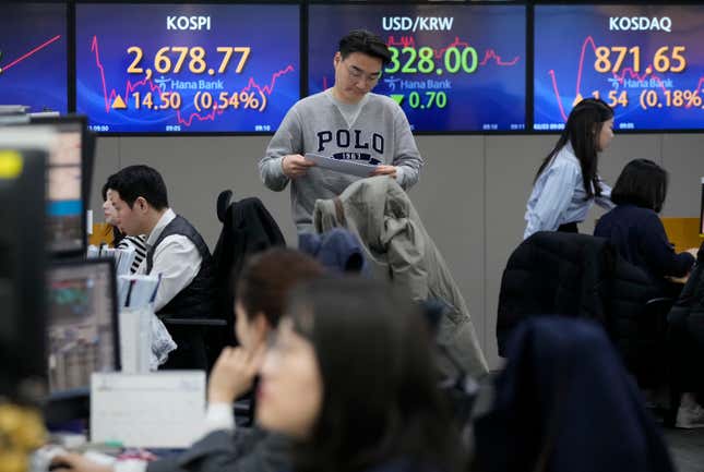 A currency trader passes by the screens showing the Korea Composite Stock Price Index (KOSPI), left, and the foreign exchange rate between U.S. dollar and South Korean won, center, at the foreign exchange dealing room of the KEB Hana Bank headquarters in Seoul, South Korea, Friday, Feb. 23, 2024. Asian markets mostly gained on Friday after Nvidia delivered another blowout quarter, setting off a rally in other technology companies that carried Wall Street to another record high. (AP Photo/Ahn Young-joon)