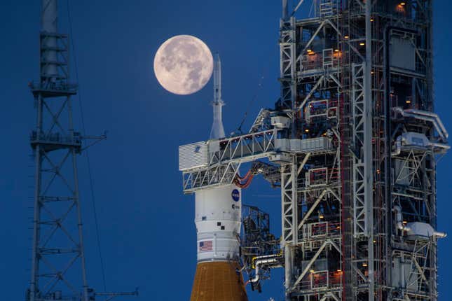 A full moon is seen behind the Artemis I Space Launch System (SLS) and Orion spacecraft, atop the mobile launcher, are prepared for a wet dress rehearsal to practice timelines and procedures for launch, at Launch Complex 39B at NASA&#39;s Kennedy Space Center in Florida on June 14, 2022. On Tuesday, Jan. 9, 2024, NASA said astronauts will have to wait until 2025 before flying to the moon and another few years before landing on it. (Cory Huston/NASA via AP)