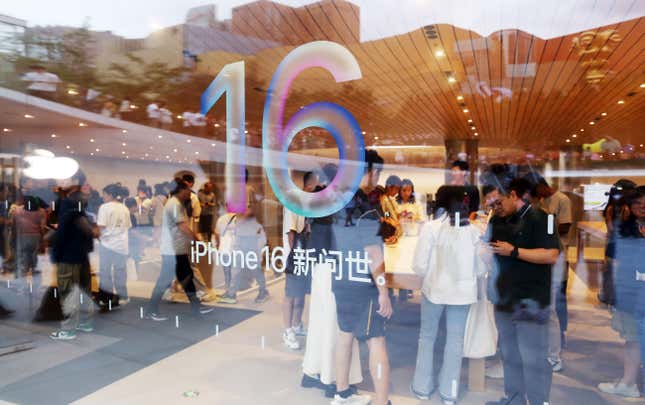 iPhone 16 logo on a store window, people can be seen inside the store