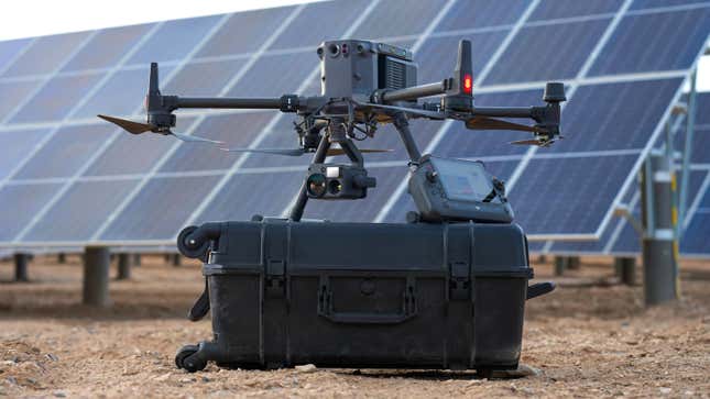 The DJI Matrice 350 RTK powered off an sitting on top of its rolling carrying case, next to a large solar array.