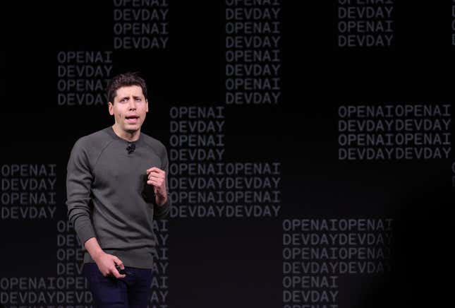 Sam Altman speaking in front of a black backdrop that has OPENAI DEVDAY printed all over it