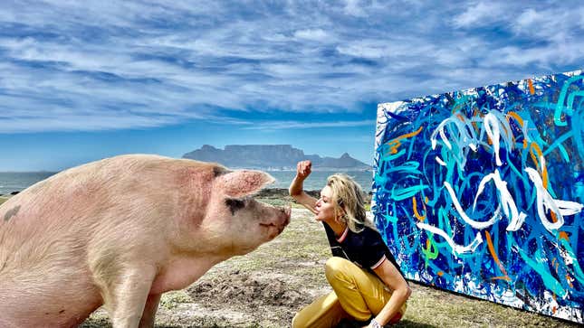 A photo of Pigcasso with her caretaker, Joanne Lefson, in front of a blue painting.